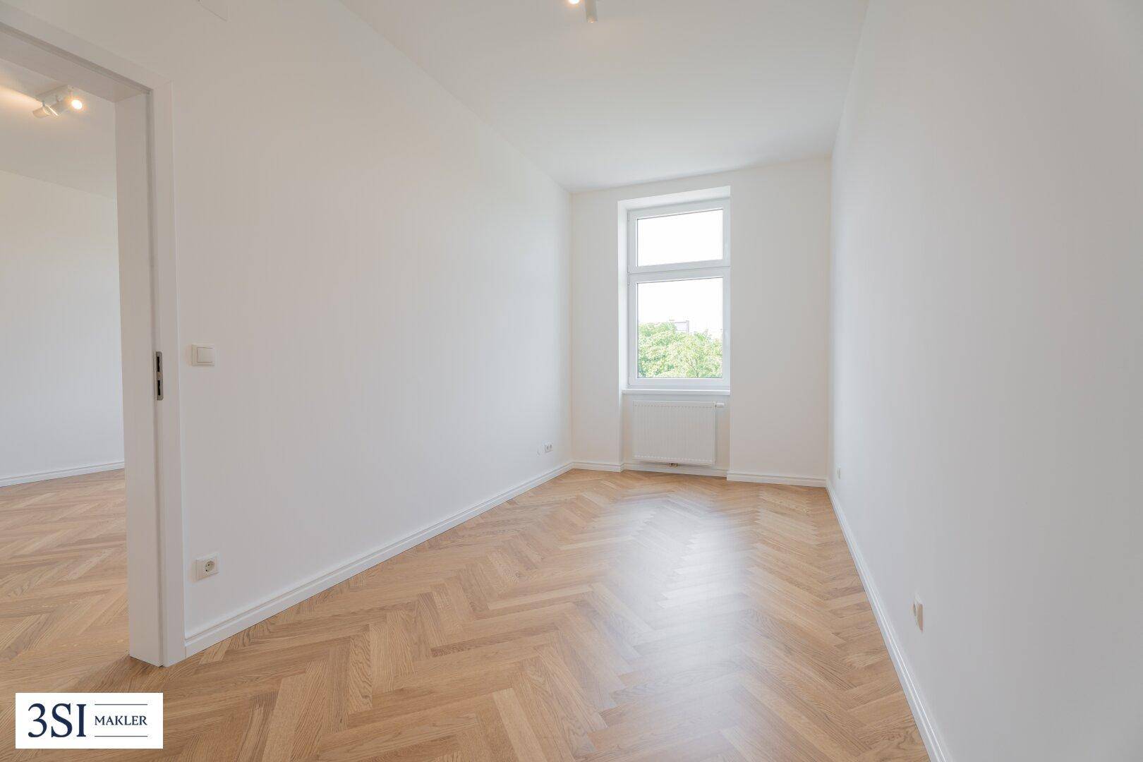 Kleineres, helles Zimmer mit Fischgrätparkett und einem Fenster, ideal als Schlaf- oder Arbeitszimmer.