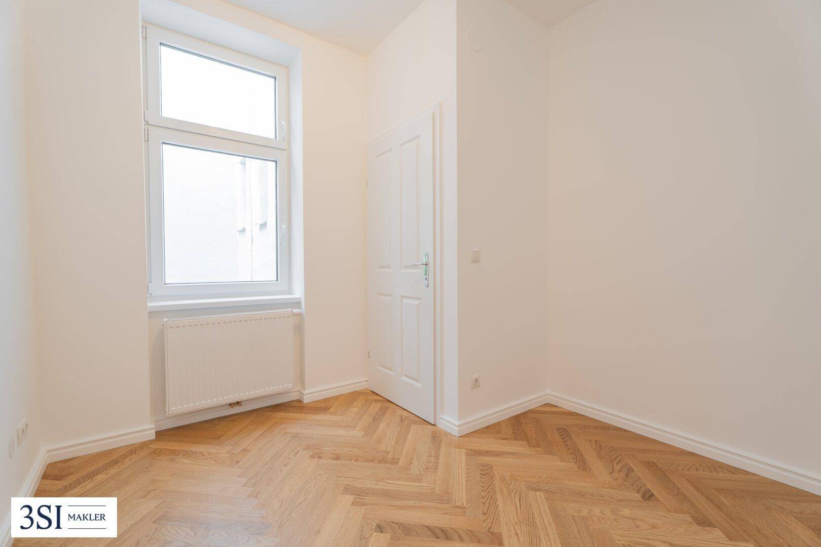 Heller Raum mit Fischgrätparkett, weiß gestrichenen Wänden und einem Fenster.