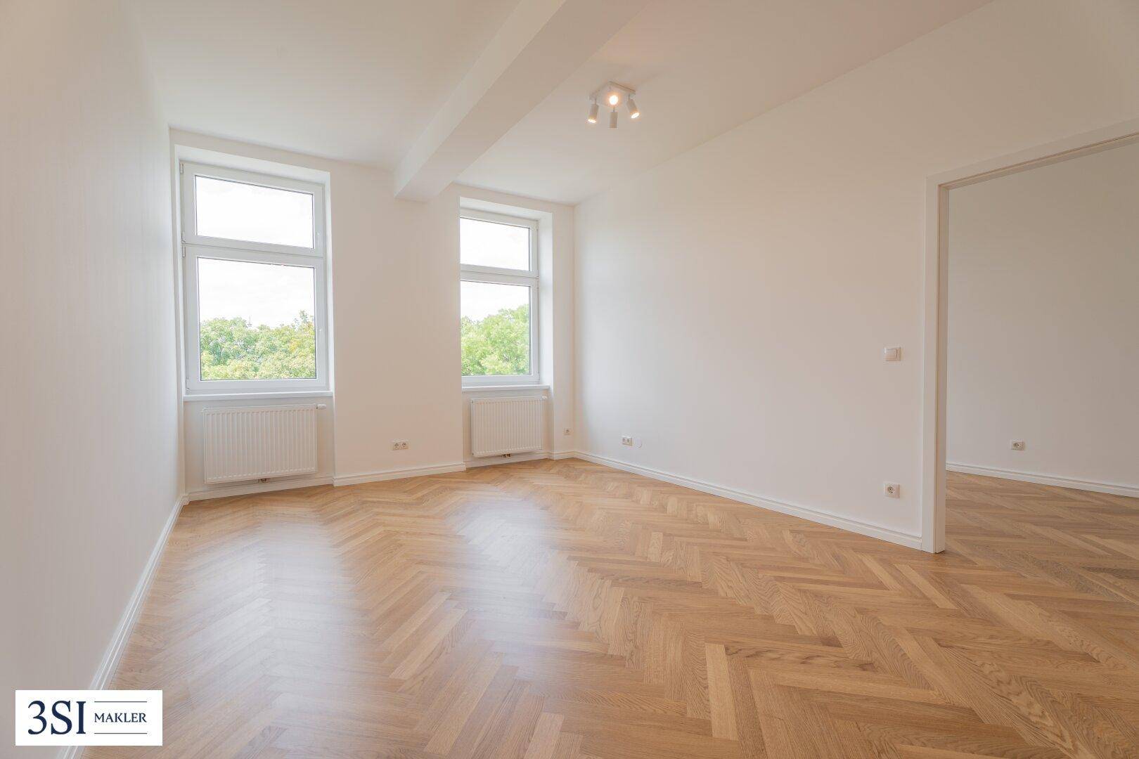 Geräumiges Schlafzimmer mit Fischgrätparkett, hellen Wänden und zwei großen Fenstern.