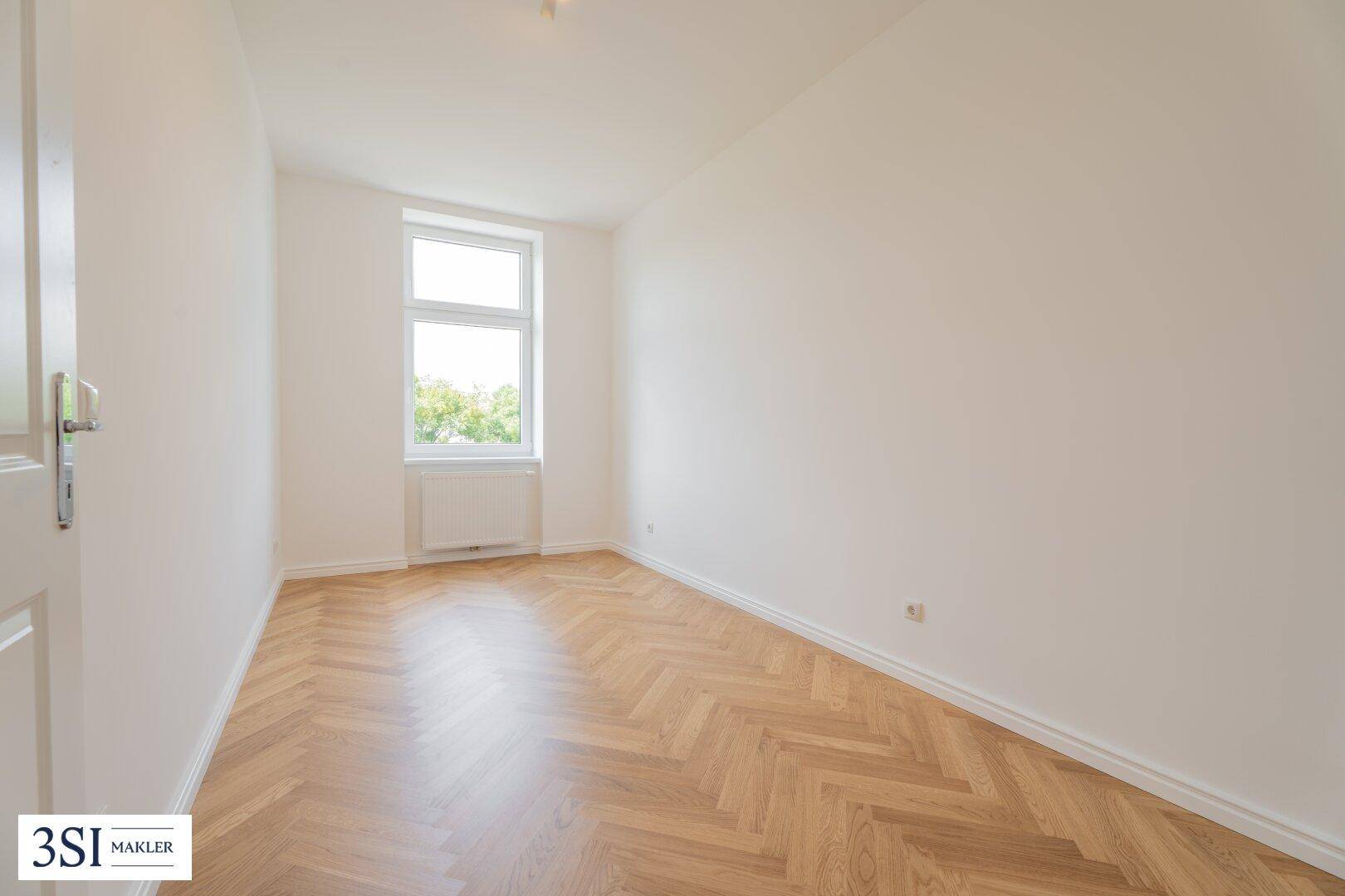 Helles Zimmer mit Parkettboden, weiß gestrichenen Wänden und einem Fenster.
