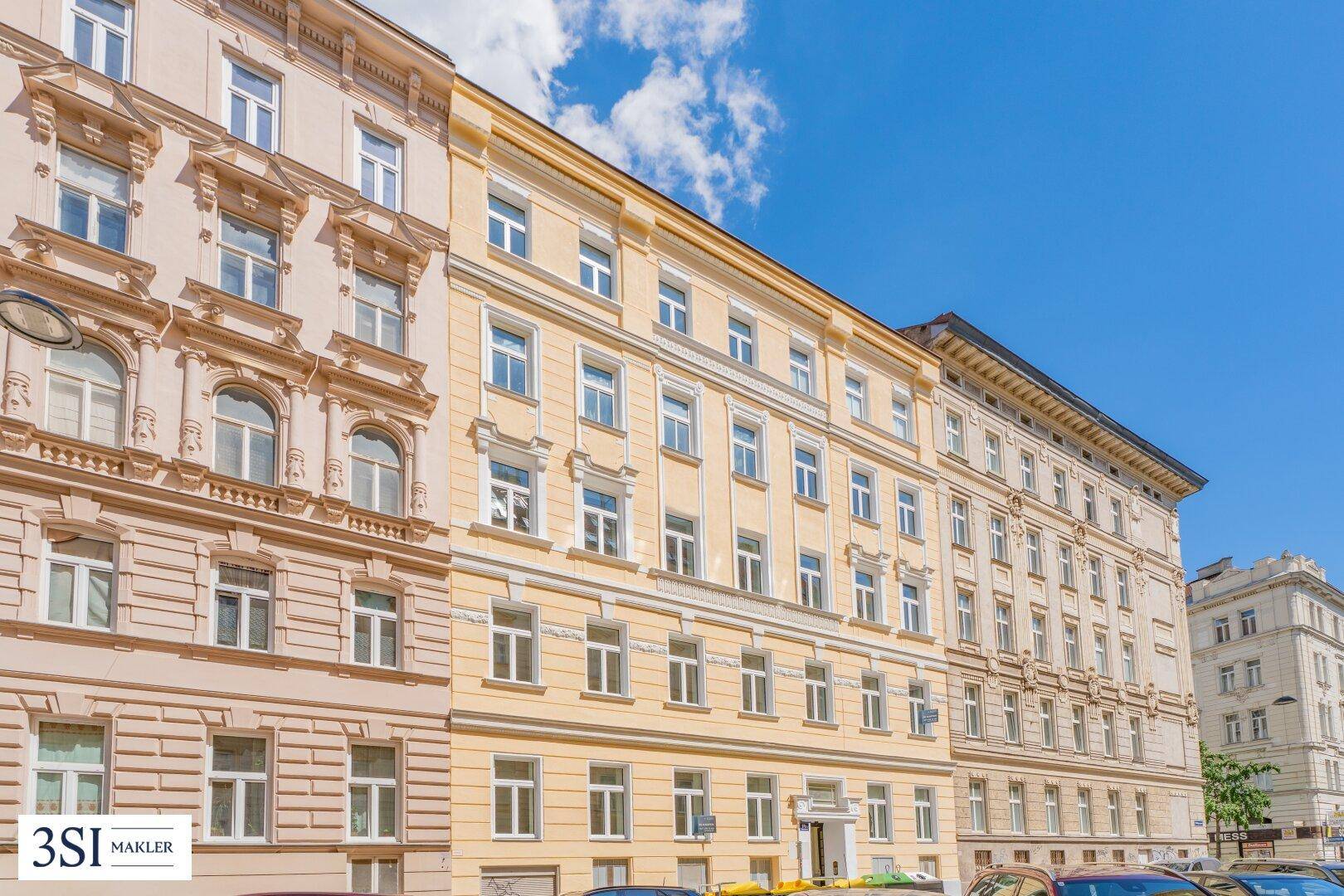 Historische Wohngebäude mit gelber und beiger Fassade unter strahlend blauem Himmel.