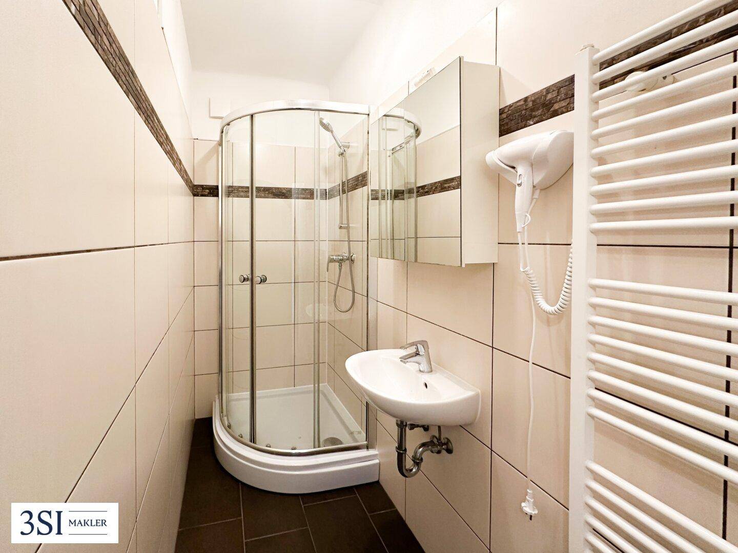Funktionales Badezimmer mit einer Eckdusche, einem Waschbecken und einem praktischen beheizten Handtuchhalter.