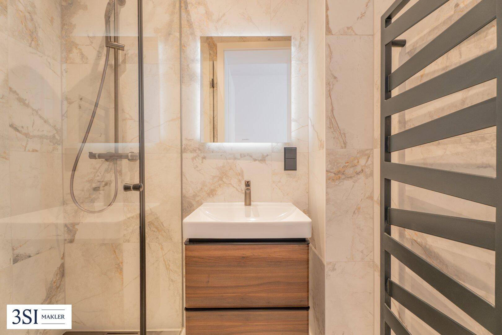 Modernes Badezimmer mit Einzelwaschbecken, beleuchtetem Spiegelschrank und Duschbereich.