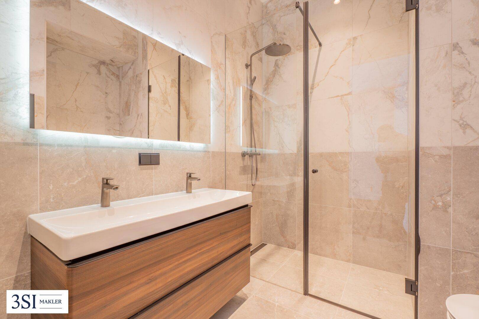 Modernes Badezimmer mit Doppelwaschbecken, beleuchtetem Spiegel und begehbarer Dusche.