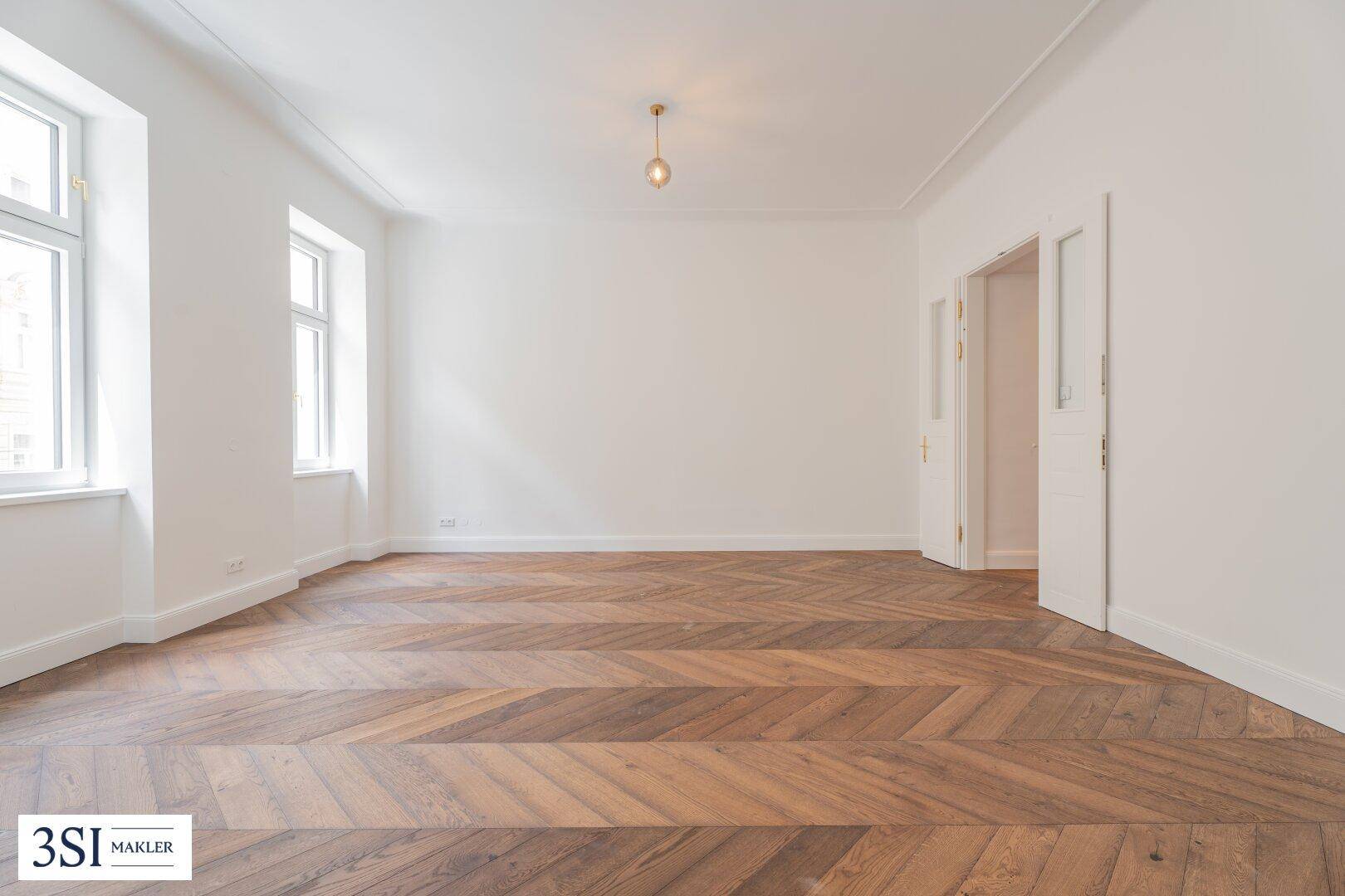 Geräumiges Wohnzimmer mit Fischgrätparkettboden, hohen Decken und viel Tageslicht.