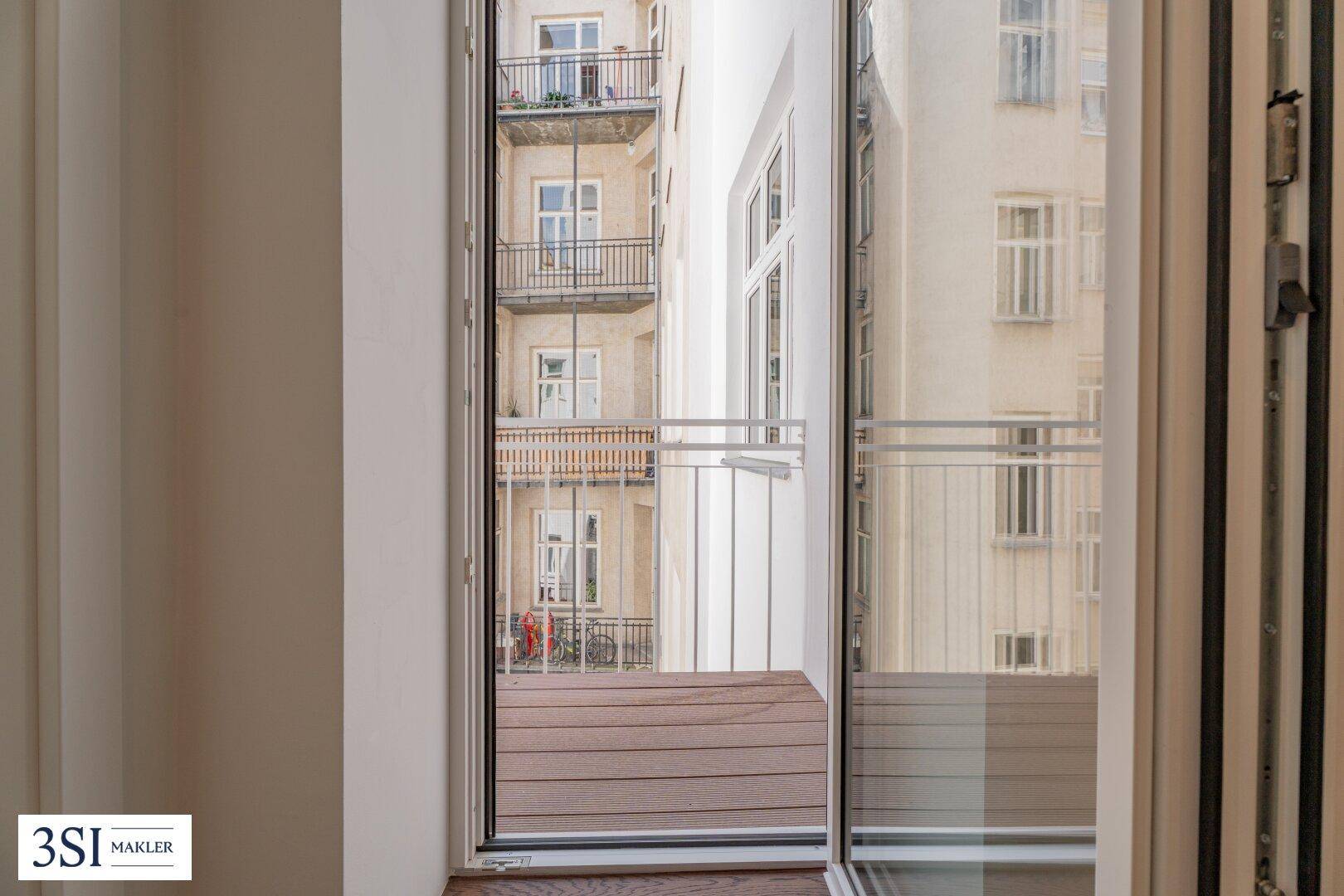 Kleiner Balkon mit Holzboden und Blick auf gegenüberliegende Gebäude mit weiteren Balkonen.