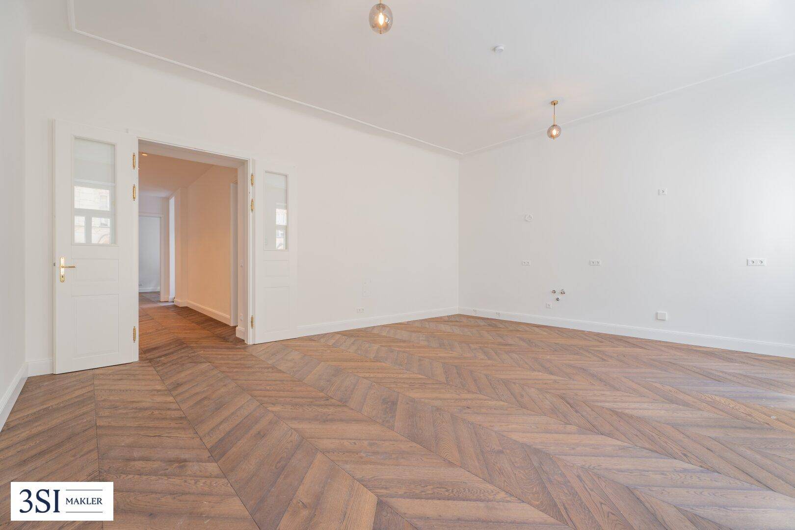 Geräumiges Wohnzimmer mit Fischgrätparkett, hohen Decken und Doppeltüren zu einem weiteren Raum.