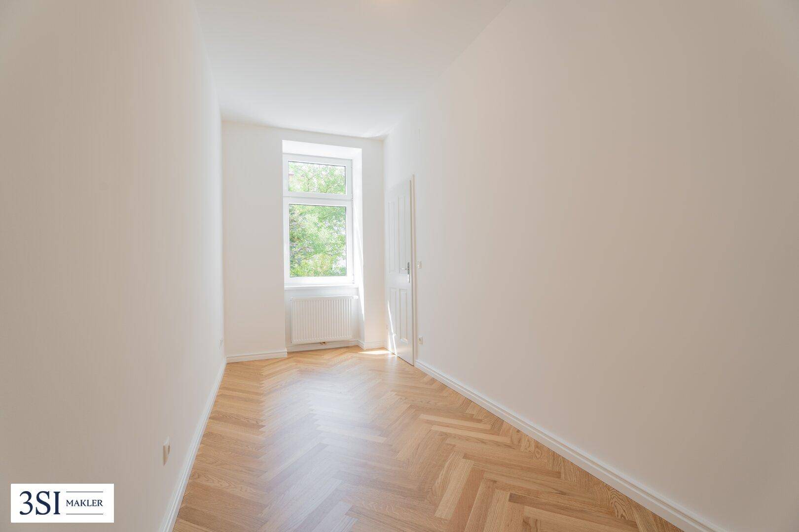Helles, leeres Zimmer mit einem Fenster und Fischgrätparkett, ideal als Schlafzimmer oder Arbeitszimmer.