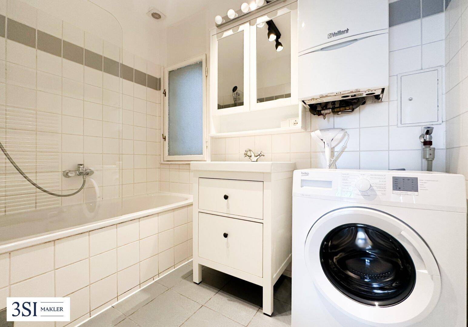 Funktionales Badezimmer mit Badewanne, Waschbecken, Spiegelschrank und Waschmaschine.