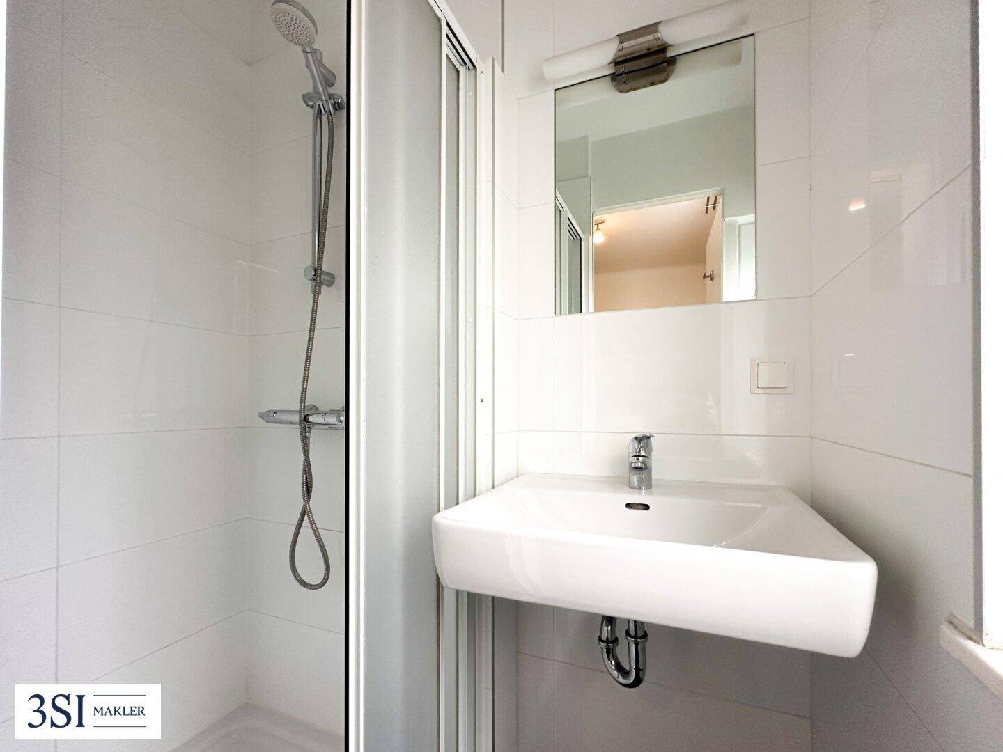 Modernes Badezimmer mit weiß gefliesten Wänden, wandmontiertem Waschbecken und Duschbereich.