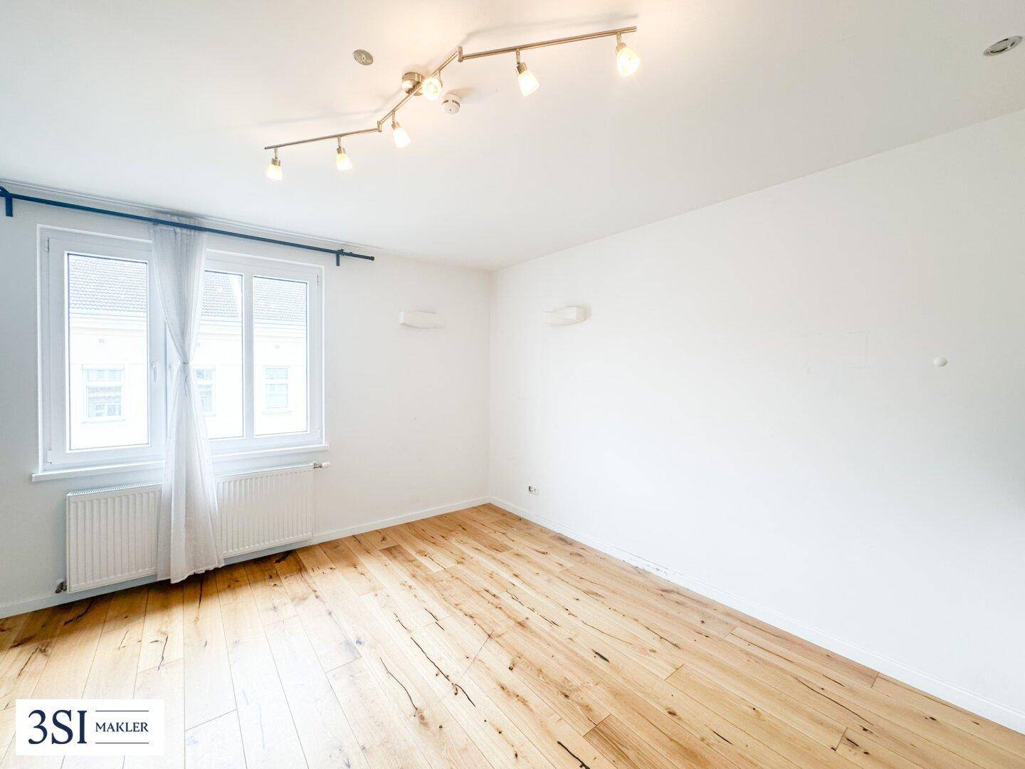 Leerer Raum mit Holzboden, weißen Wänden und großen Fenstern, bereit zur Einrichtung.