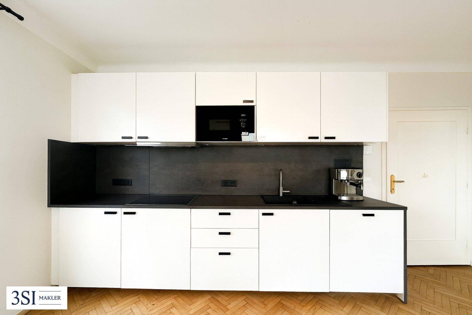 Moderne Einbauküche mit weißen Schränken, dunkler Arbeitsplatte und integrierten Geräten.