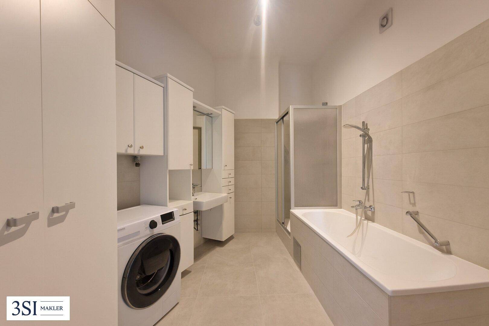 Modernes Badezimmer mit Badewanne, Duschkabine, Waschmaschine und hellen Fliesen.