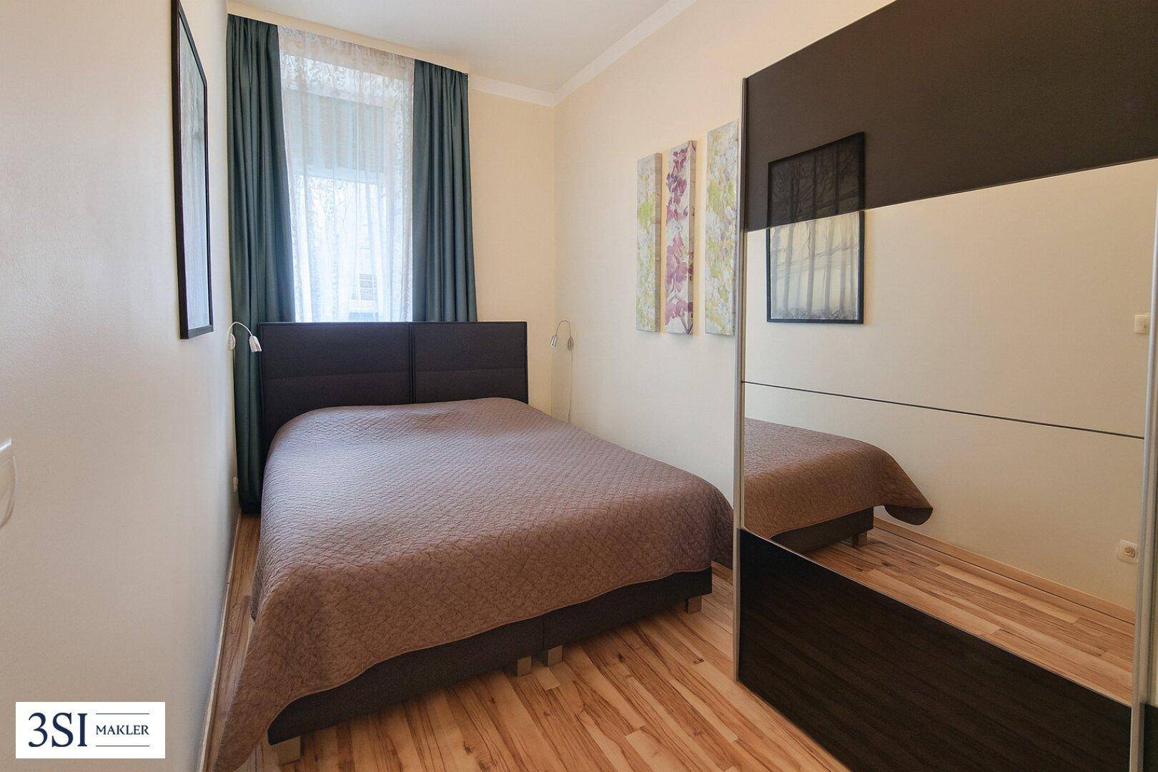 Schlafzimmer mit Doppelbett, Holzboden und einem großen Spiegelschrank.