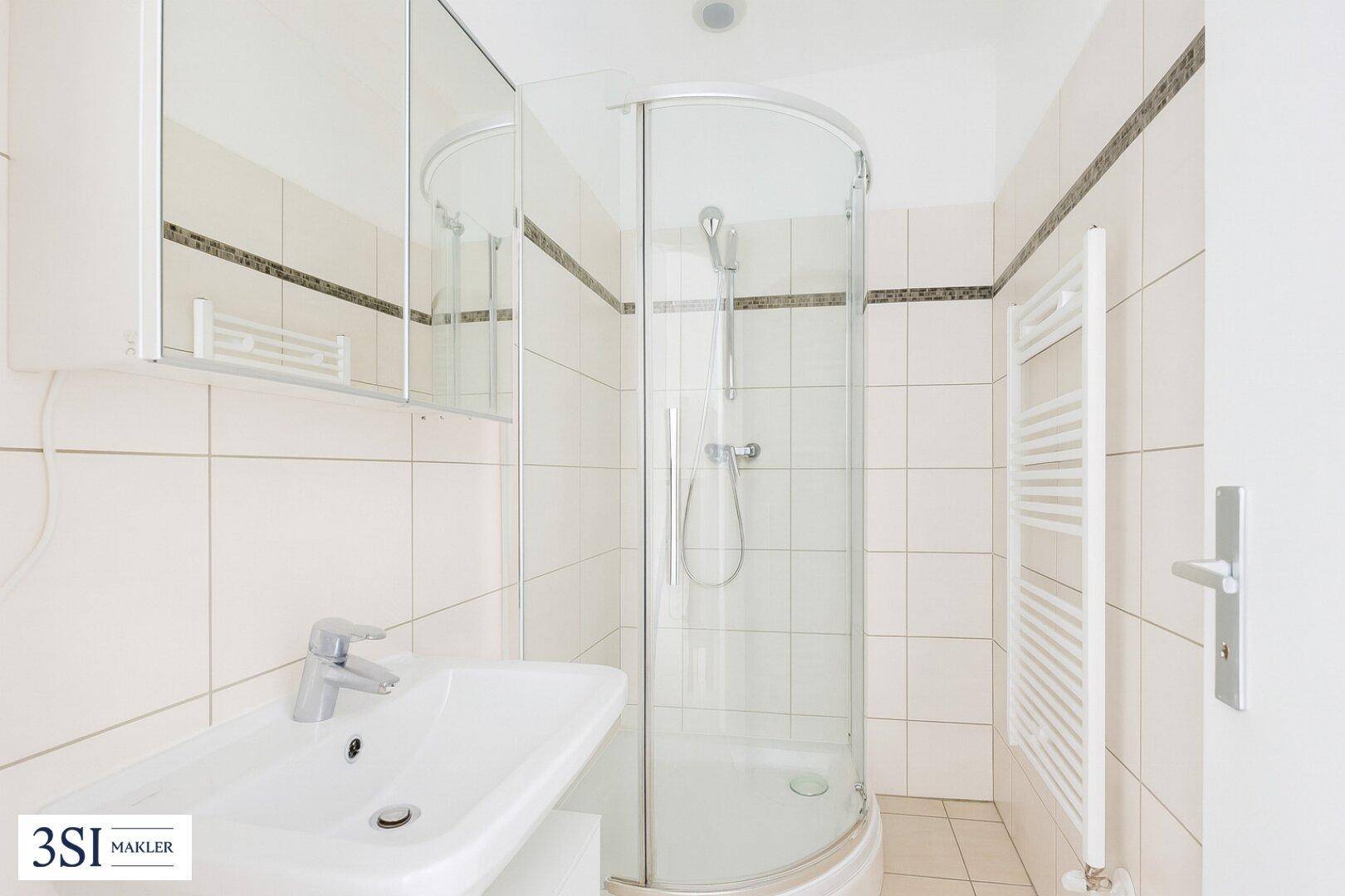 Helles Badezimmer mit Duschkabine, Waschbecken und beheiztem Handtuchhalter.