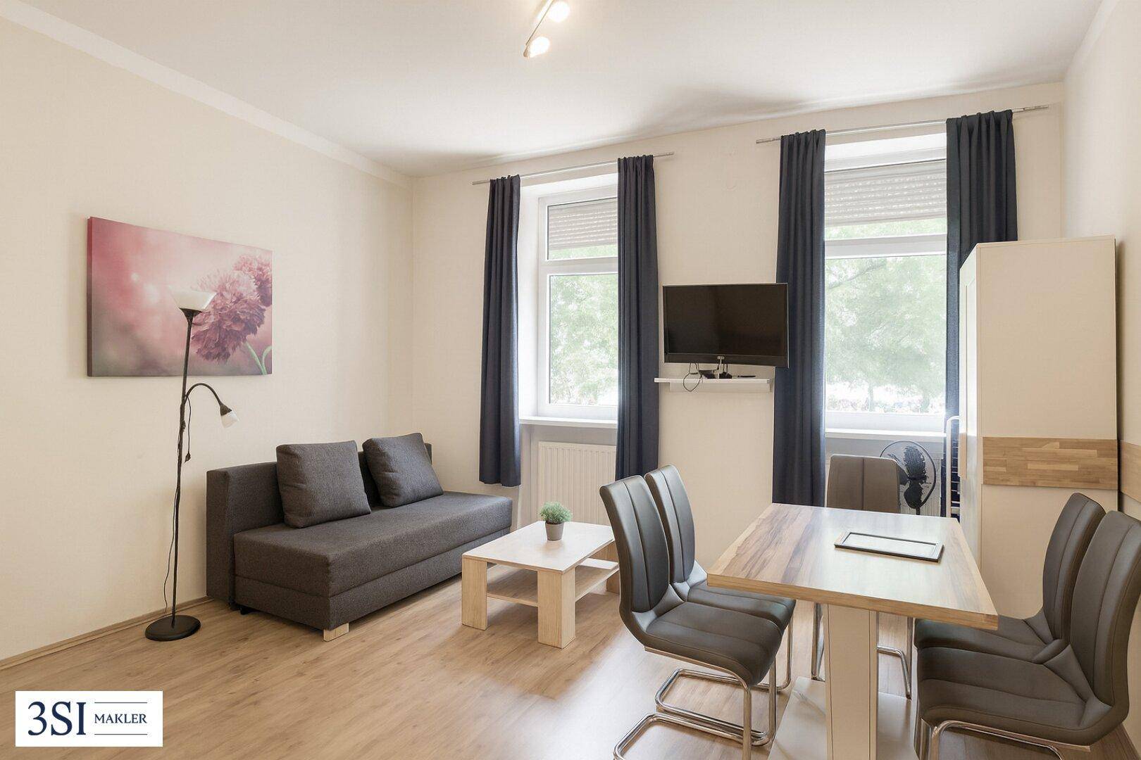 Heller Wohn- und Essbereich mit Holzboden, einem Sofa, Esstisch und großen Fenstern mit dunklen Vorhängen.