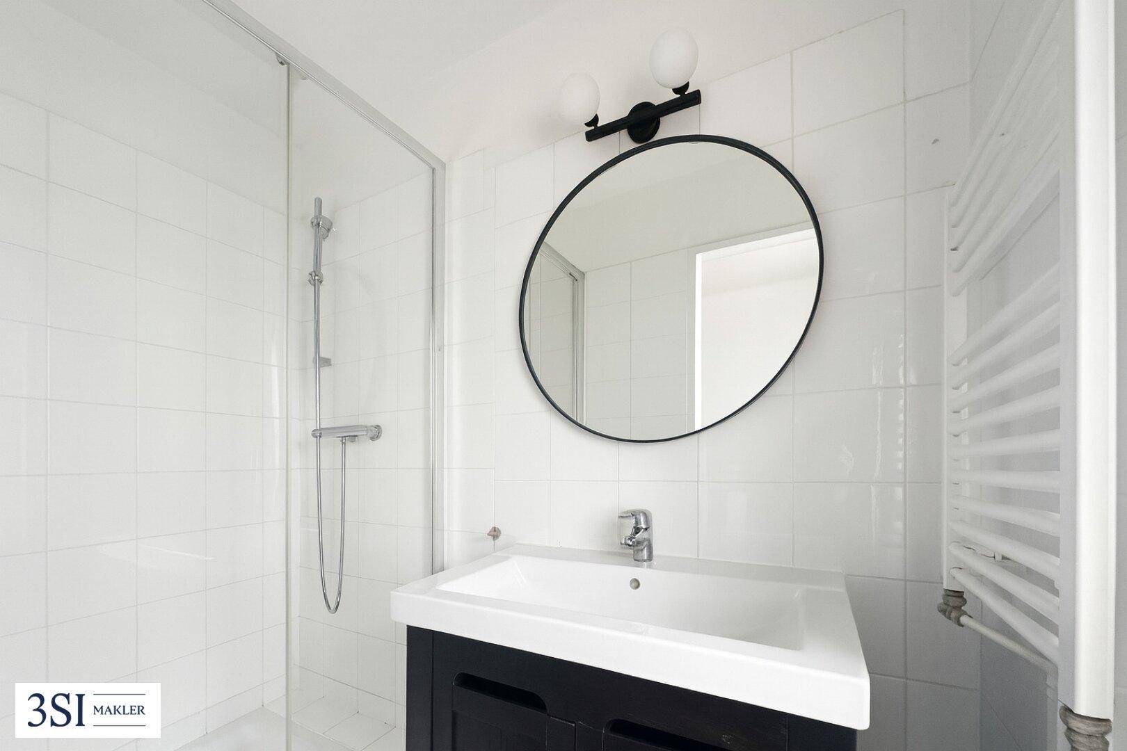 Modernes Badezimmer mit weiß gefliesten Wänden, Dusche, Einzelwaschbecken und beheiztem Handtuchhalter.