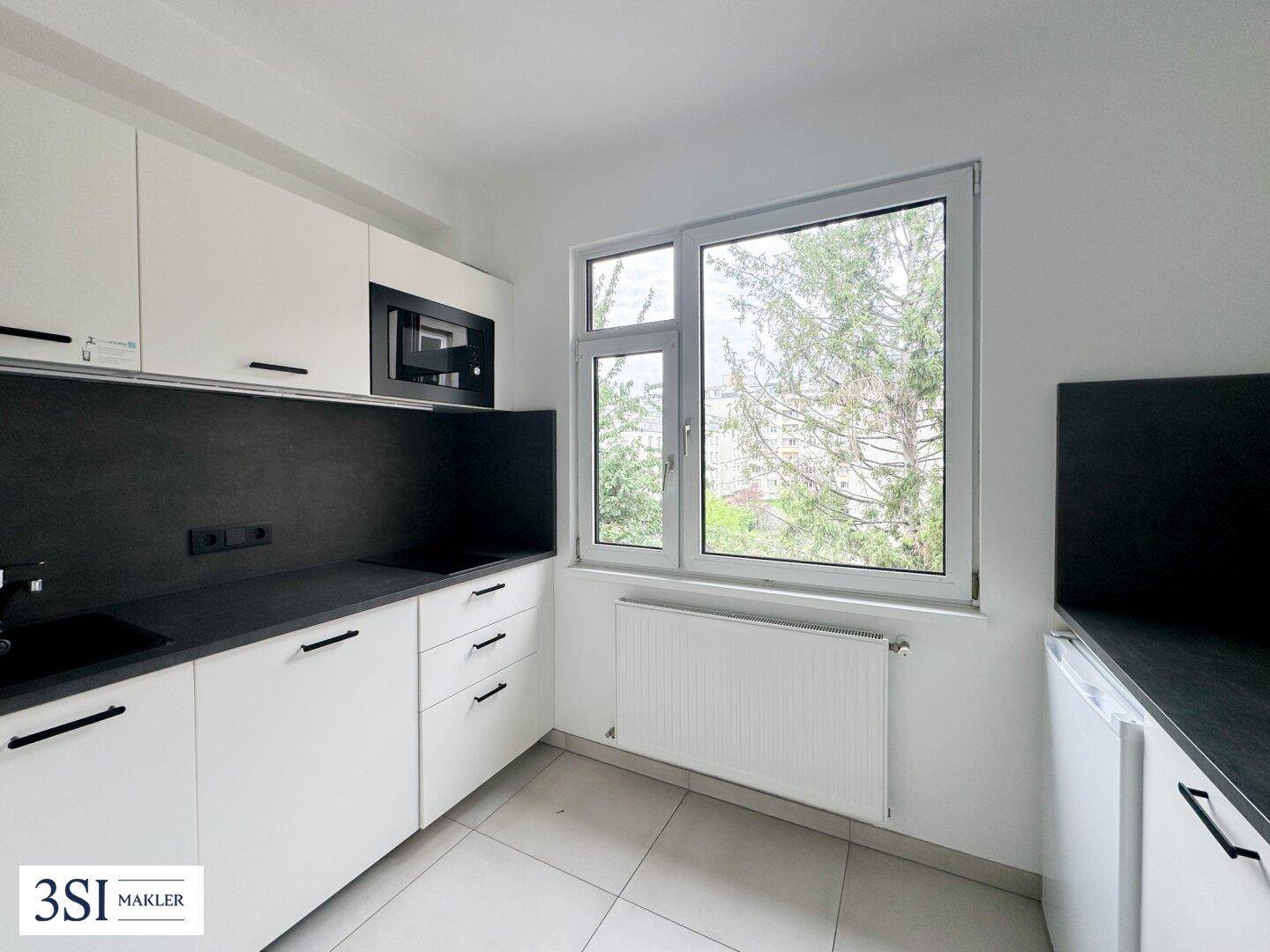Moderne Küche mit weißen Schränken, dunkler Arbeitsplatte und Fensterblick ins Grüne.