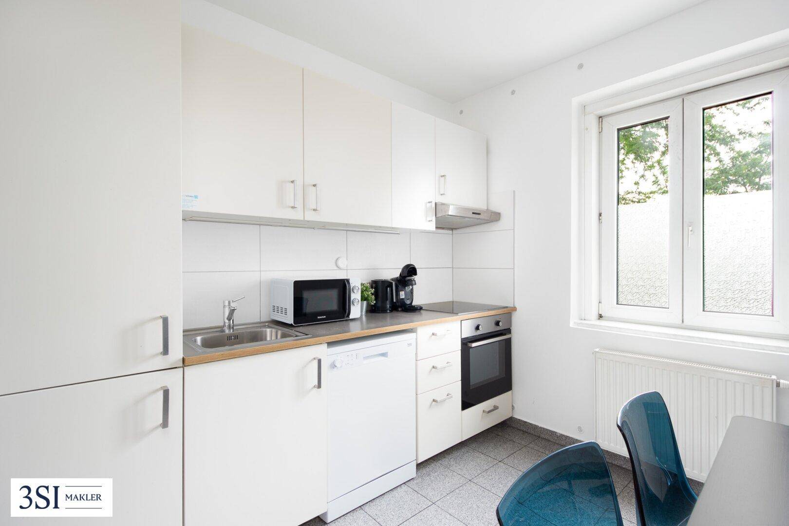 Funktionale Küche mit weißen Schränken, integrierten Geräten und einem Fenster für Tageslicht.