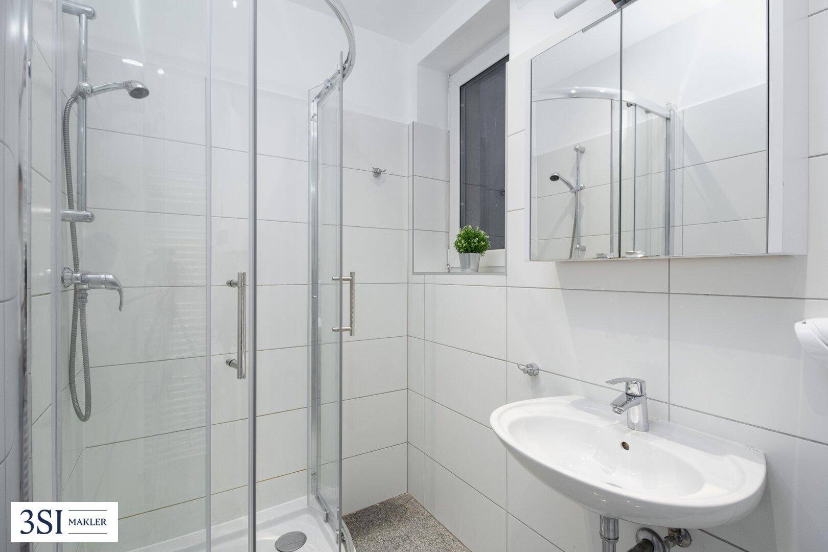 Helles Badezimmer mit weiß gefliesten Wänden, Dusche und Spiegelschrank.