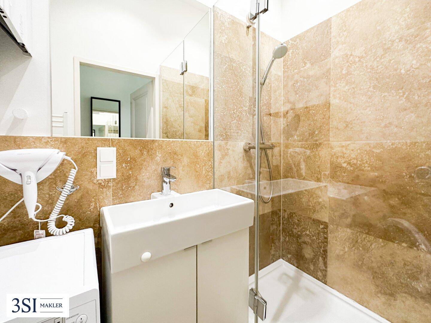 Funktionales Badezimmer mit Duschkabine, modernem Waschbecken und beigefarbenen Fliesen an den Wänden.