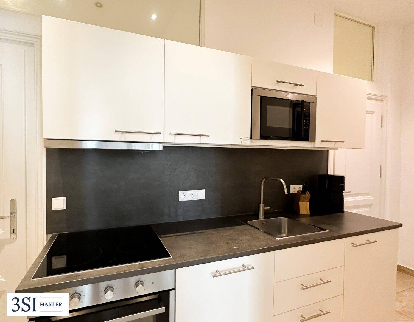 Kompakte, moderne Küche mit weißen Schränken, Induktionskochfeld, Backofen und integrierter Mikrowelle.