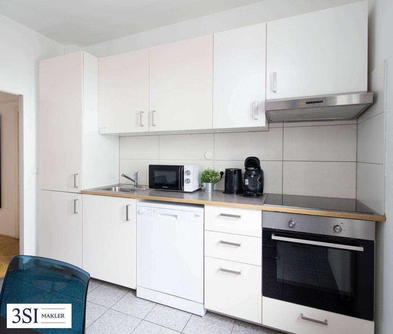 Moderne Einbauküche mit weißen Schränken, integriertem Backofen, Geschirrspüler und Mikrowelle.