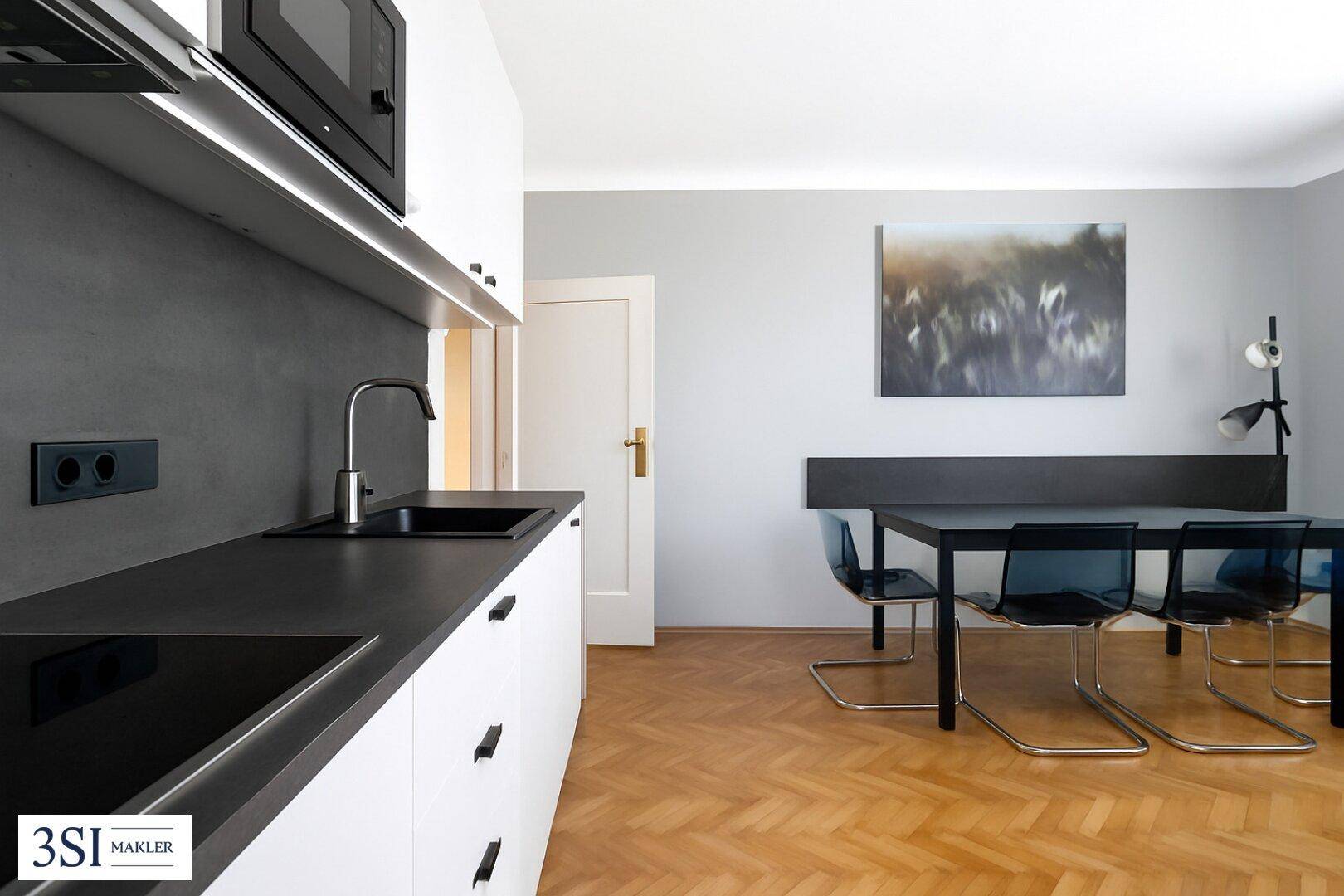 Moderne Küche mit dunklen Arbeitsplatten und integriertem Kochfeld, kombiniert mit einem Essbereich und Holzboden.