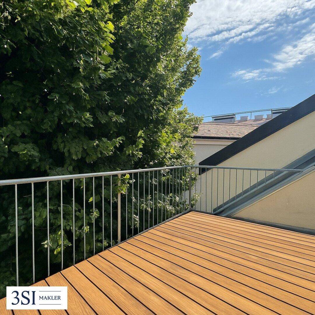 Holzterrasse mit Metallgeländer und Blick ins Grüne unter einem bewölkten Himmel.