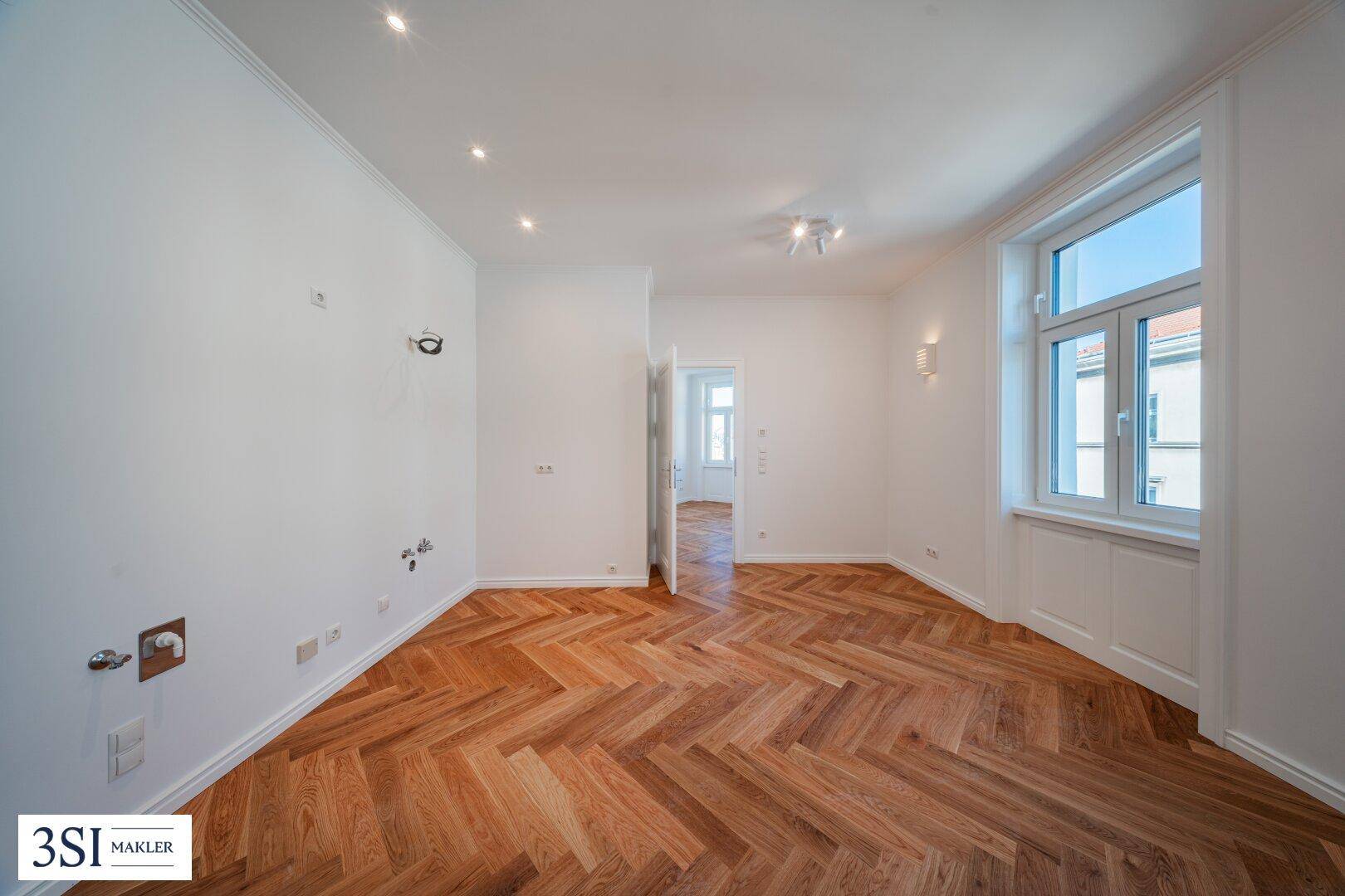 Heller Raum mit Fischgrätparkett und vorbereiteten Anschlüssen an der Wand.
