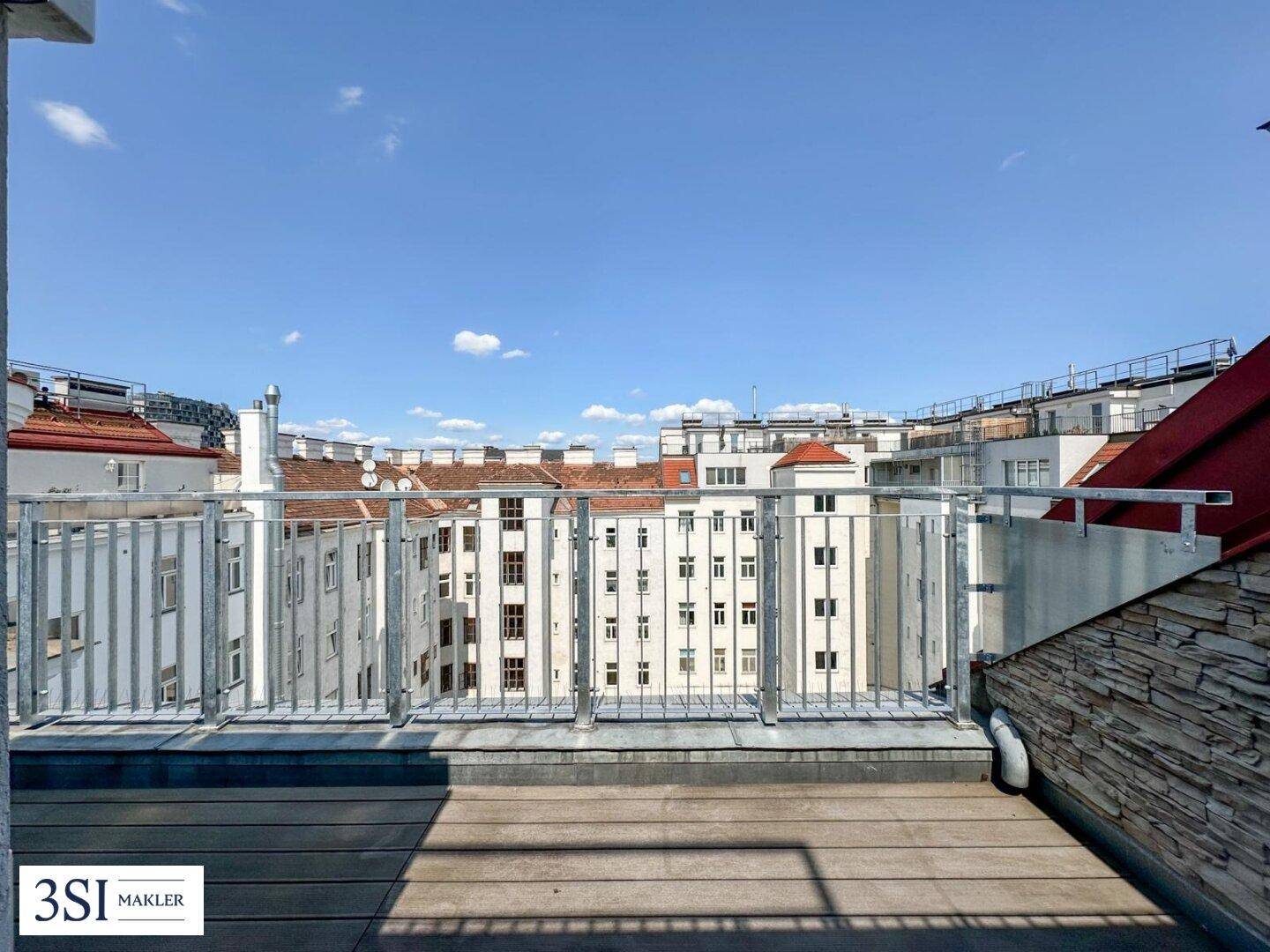 Dachterrasse mit Metallgeländer und Blick auf die umliegenden Gebäude unter blauem Himmel.