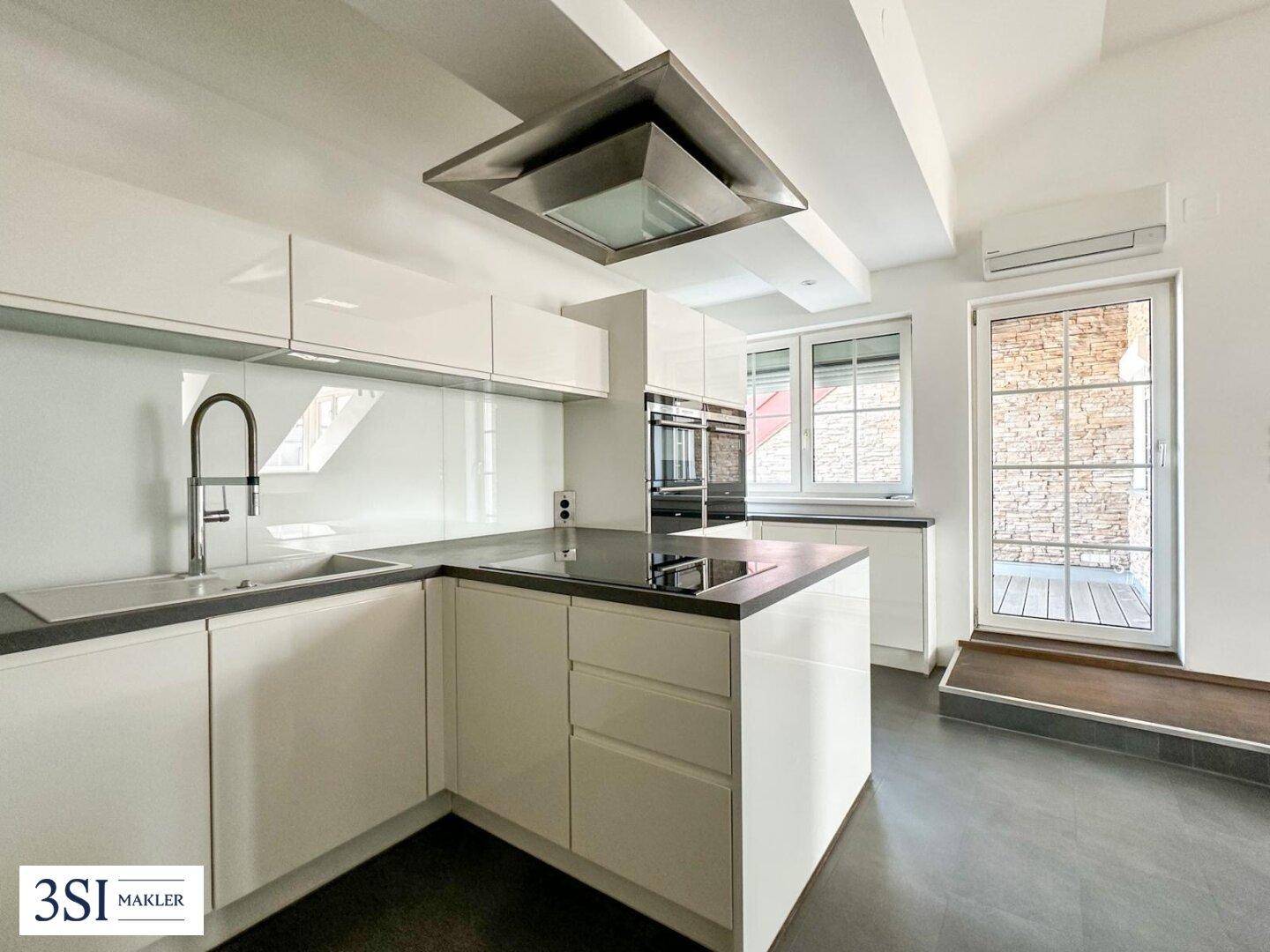 Helle, moderne Küche mit weißen Schränken, dunkler Arbeitsplatte und direktem Zugang zur Terrasse.
