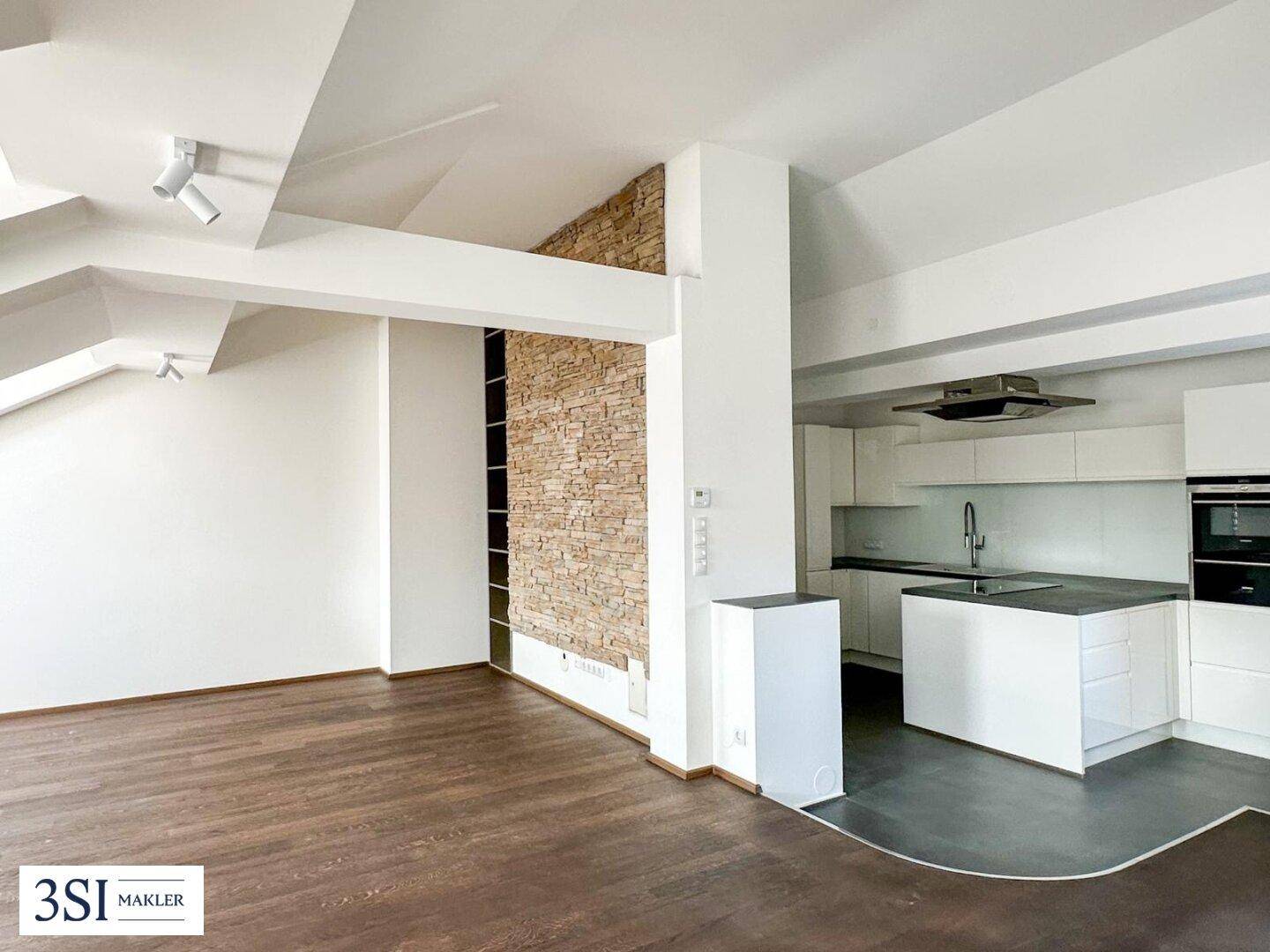 Offener Wohnbereich mit Steinwand, dunklem Holzboden und Blick auf die moderne Küche.
