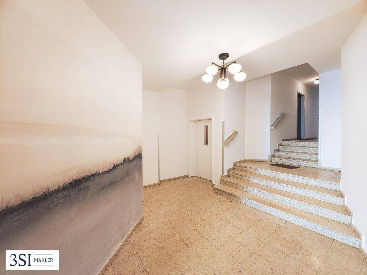 Heller Eingangsbereich mit Steintreppe, Fliesenboden und modernem Deckenlicht.