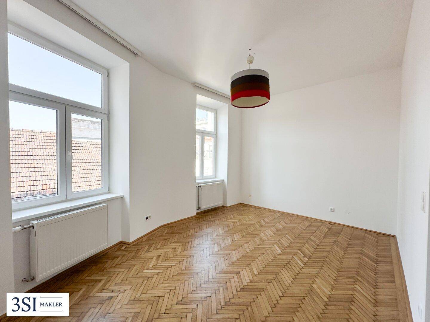 Helles Schlafzimmer mit Fischgrätparkett, hohen Fenstern und einer modernen Deckenleuchte.
