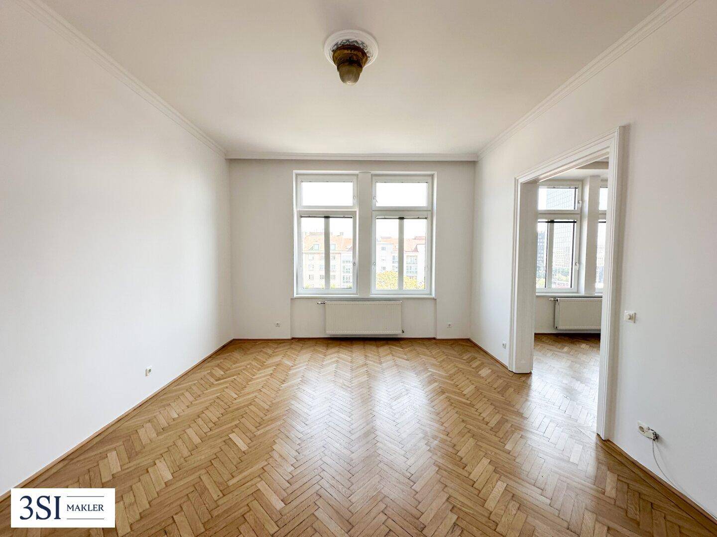 Großes, helles Zimmer mit Fischgrätparkett und hohen Decken in einem Altbau.