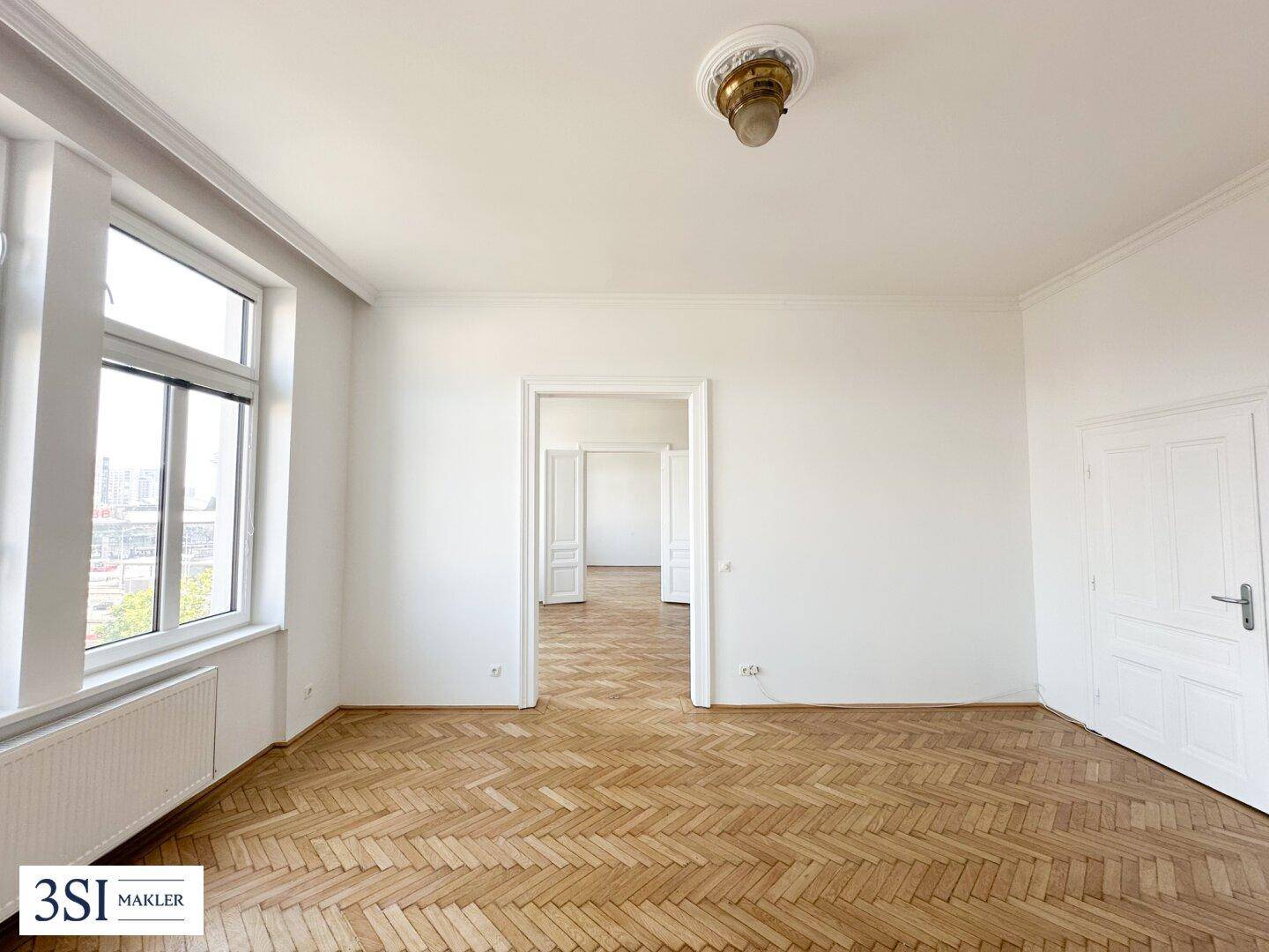 Geräumiges Zimmer mit Fischgrätparkett, hohen Fenstern und klassischer Deckenverzierung.