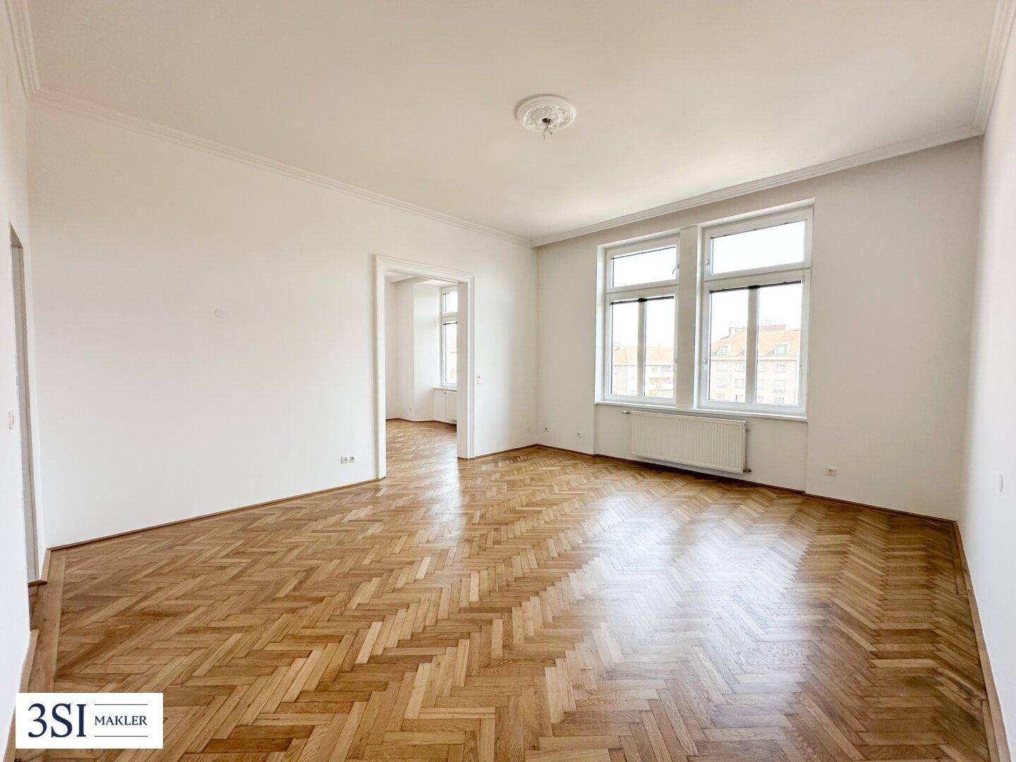 Geräumiges Wohnzimmer mit klassischem Fischgrätparkett und großen Fenstern.