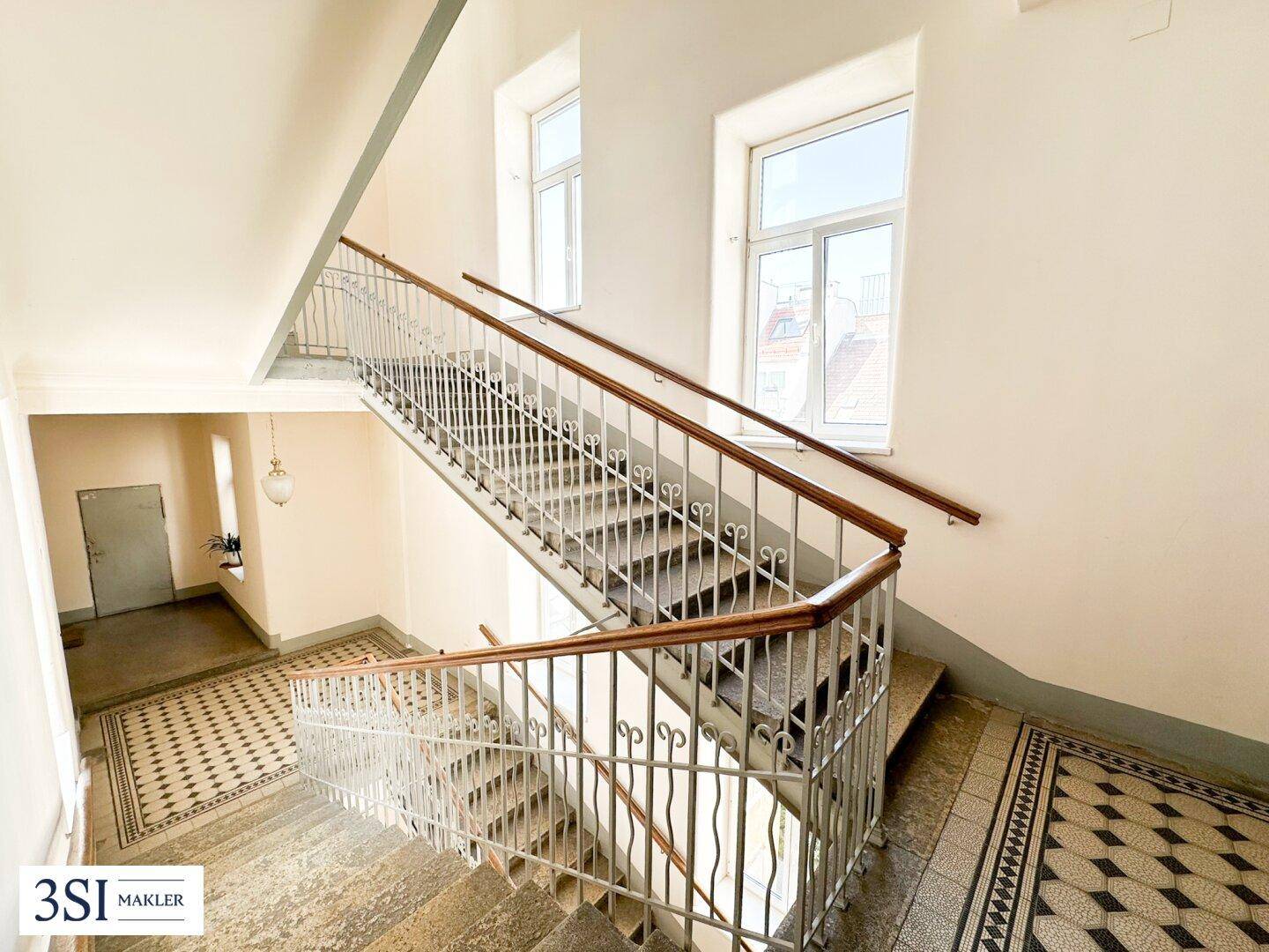 Historisches Treppenhaus mit kunstvollem Geländer und gemusterten Fliesen.
