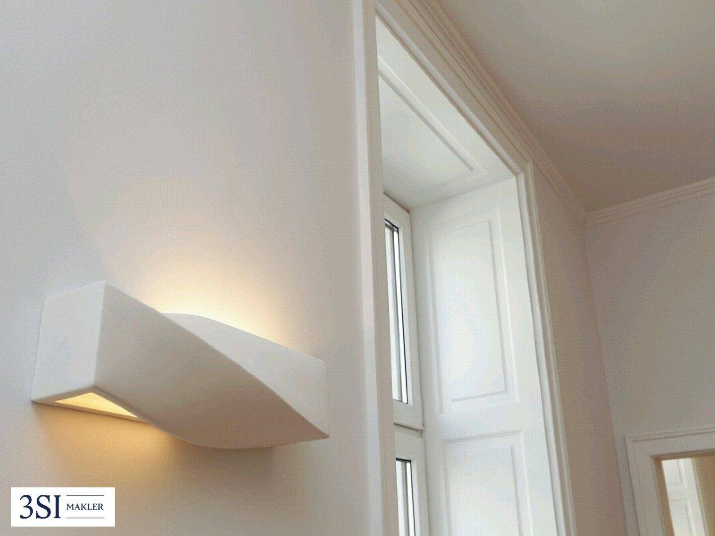 Moderne Wandleuchte an einer weißen Wand neben einem Fenster mit eleganten Fensterläden.