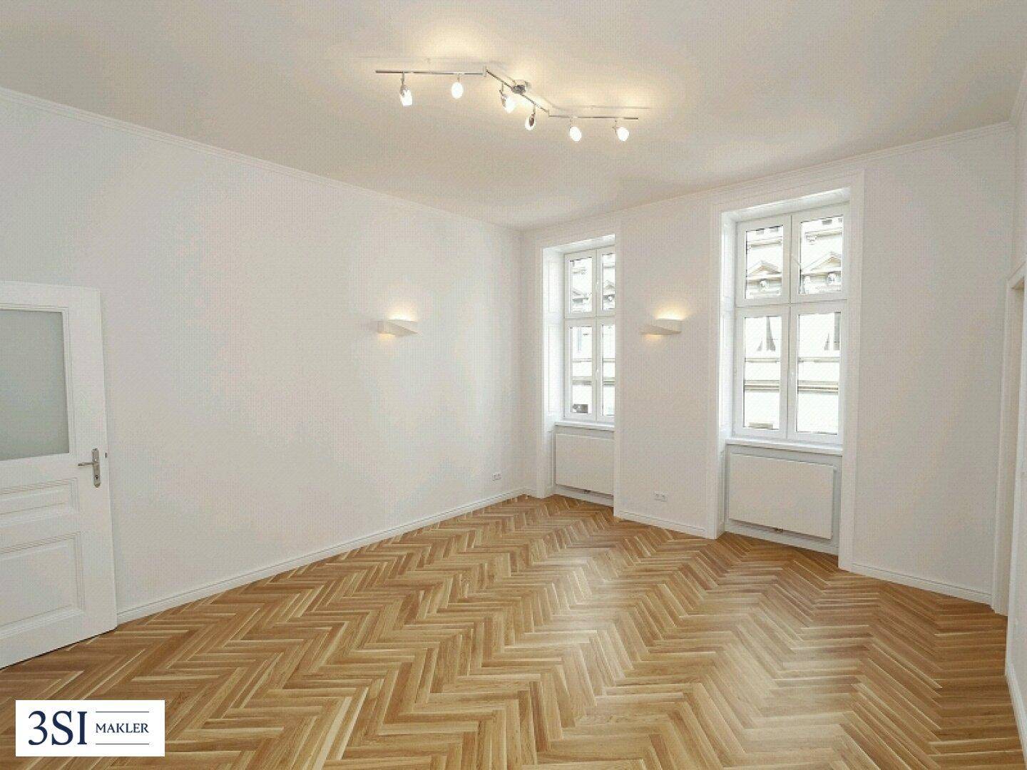 Heller, leerer Raum mit elegantem Fischgrätparkettboden und zwei großen Fenstern.