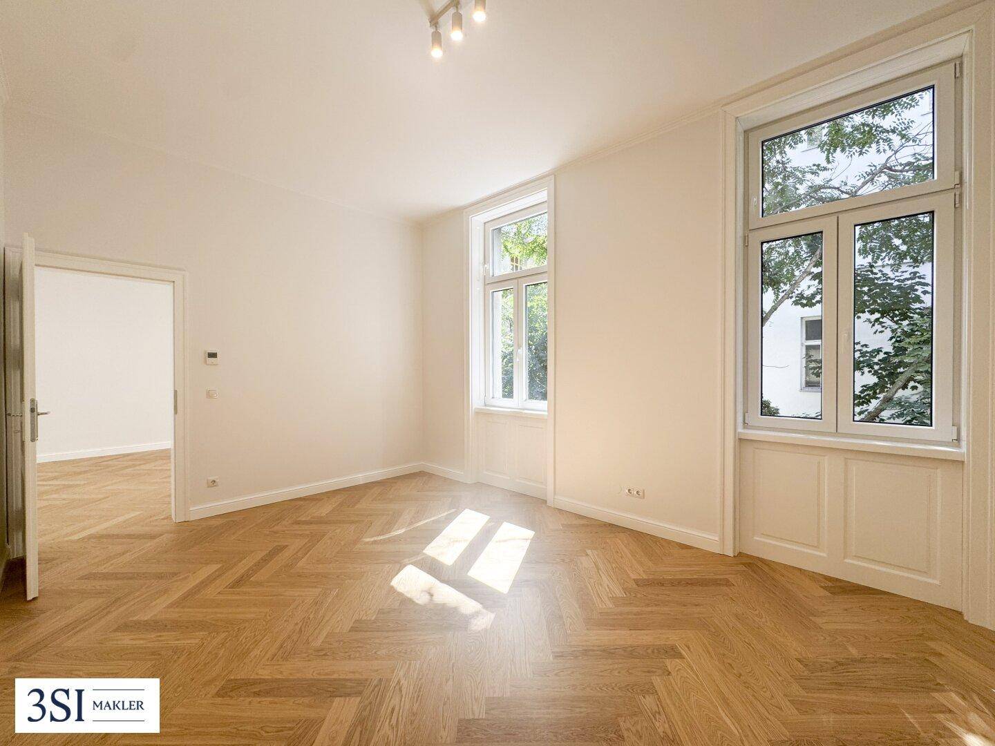 Heller Wohnraum mit Fischgrätparkett und großen Fenstern, die viel Sonnenlicht hereinlassen.