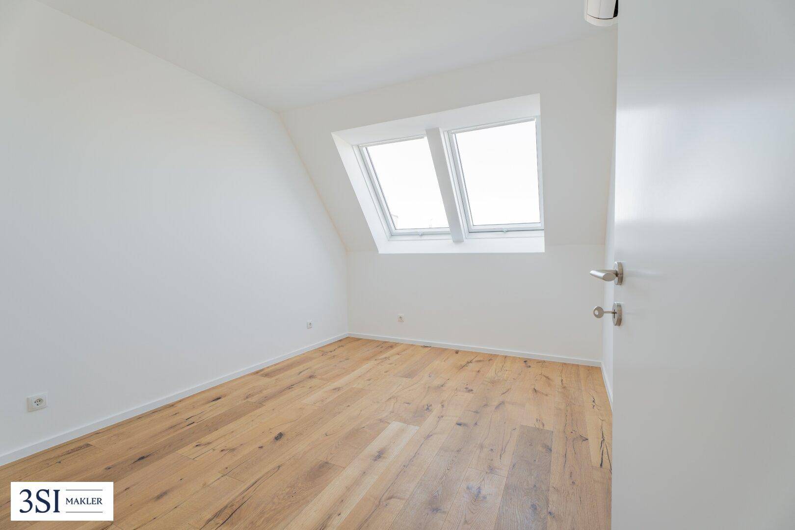 Lichtdurchflutetes Zimmer im Dachgeschoss mit Holzboden und zwei großen Dachfenstern.