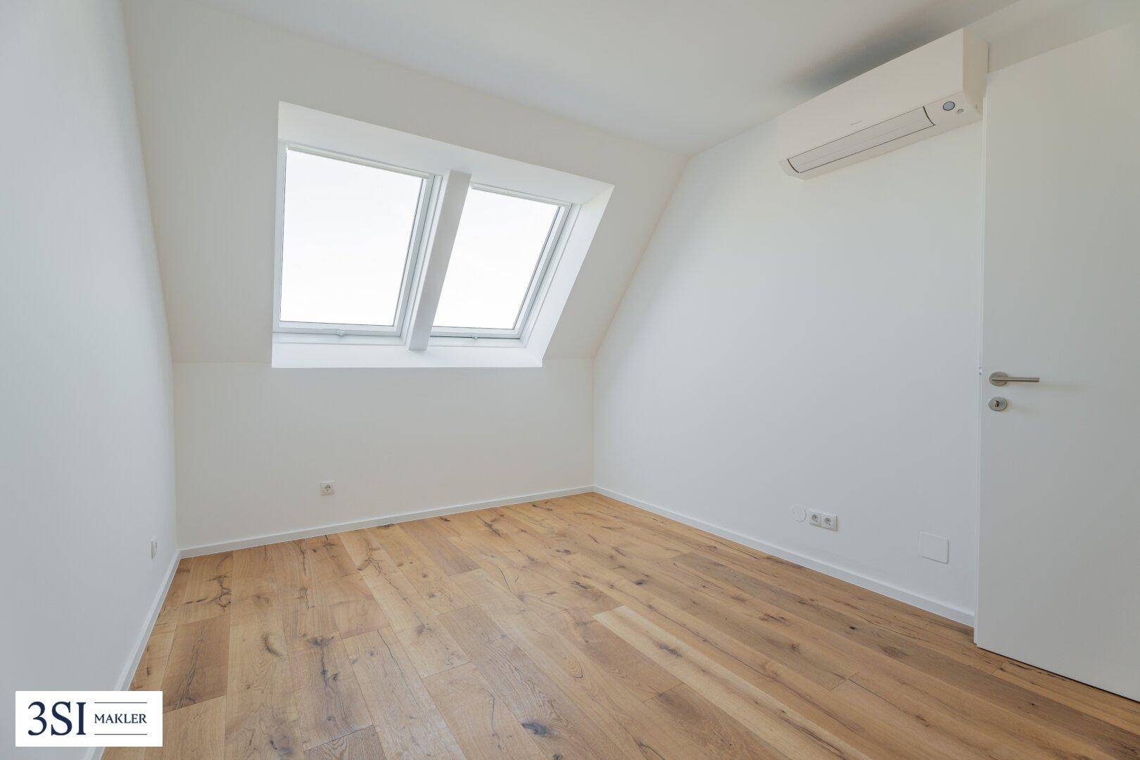 Modernes Dachzimmer mit Holzboden, Klimaanlage und schrägen Wänden mit Dachfenstern.