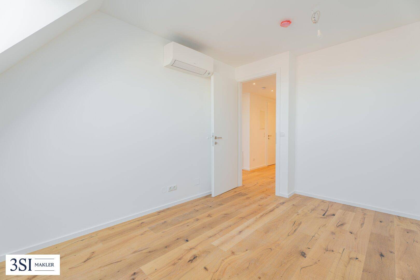 Helles Zimmer im Dachgeschoss mit Holzboden, Klimaanlage und Zugang zu einem weiteren Raum.