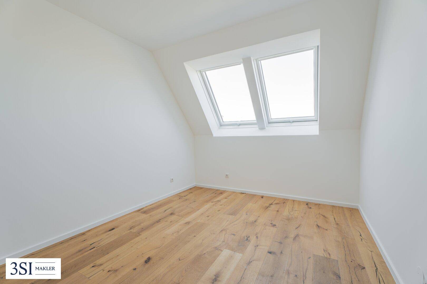 Ruhiges Dachzimmer mit Holzboden und zwei großen Dachfenstern, ideal als Schlaf- oder Arbeitszimmer.