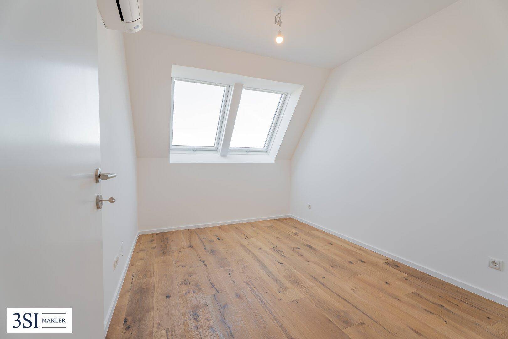 Modernes Dachzimmer mit Holzboden, Klimaanlage und schrägen Wänden mit Dachfenstern.