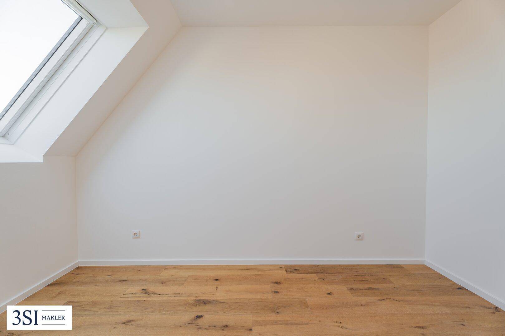 Leeres Zimmer im Dachgeschoss mit Holzboden und einem einzelnen Dachfenster, bereit zur Einrichtung.