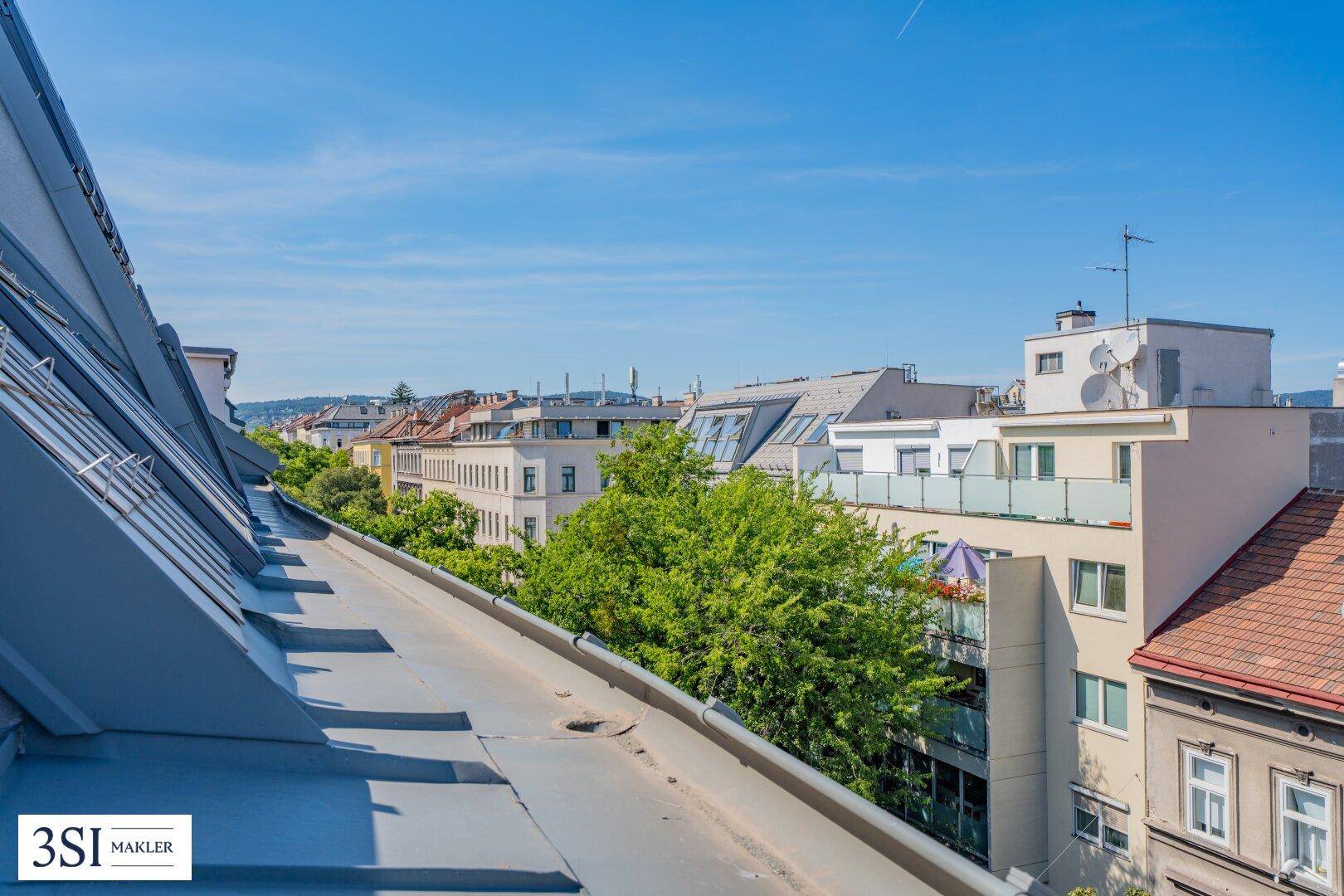 Dachlandschaft der Stadt mit Blick auf umliegende Gebäude und grüne Baumkronen.