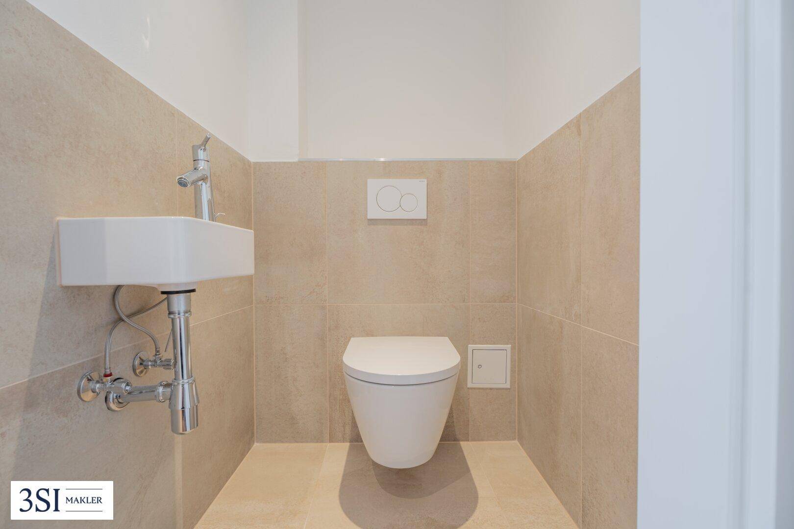 Separates WC mit wandhängender Toilette, kleinem Waschbecken und beigefarbenen Fliesen.